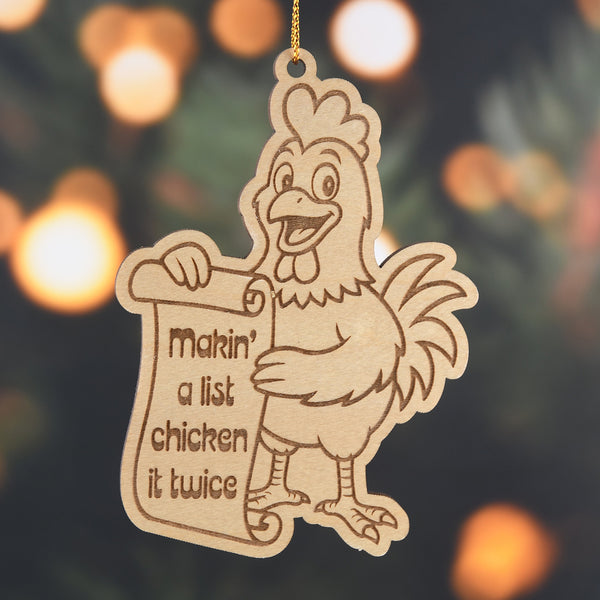 Wooden ornament of a chicken holding a sign with text, against a blurred Christmas tree background.