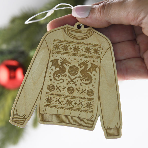 Wood engraved sweater ornament with a design featuring a D20 die and dragons, held in a woman's hand