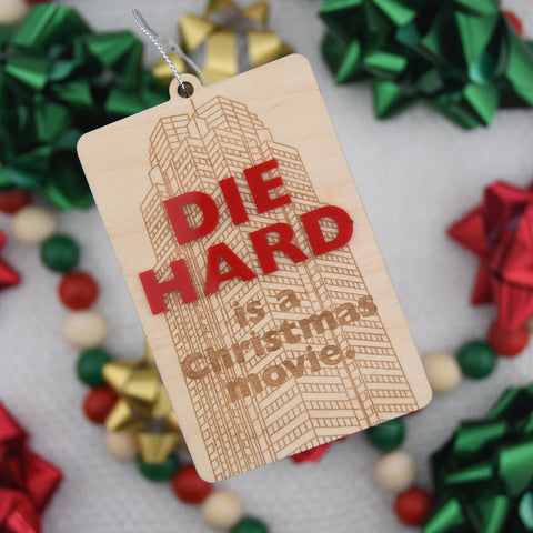 Wooden tag with 'Die Hard is a Christmas movie' text, surrounded by festive ribbons and decorations.