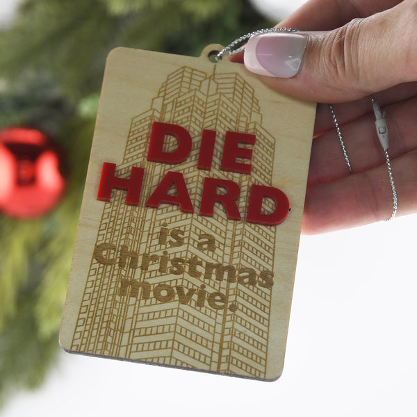 Wooden tag with 'Die Hard is a Christmas movie' text held by a hand against a blurred background