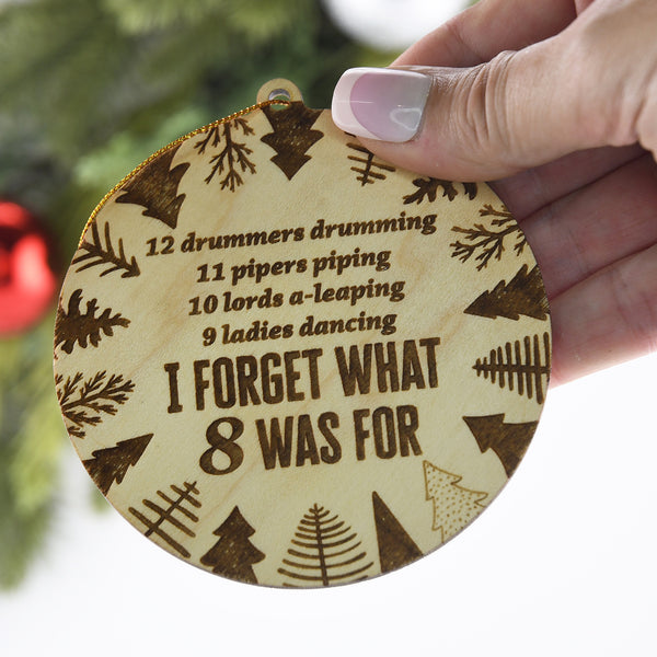 Wooden ornament with Christmas carol text held by a hand against a blurred Christmas tree background.