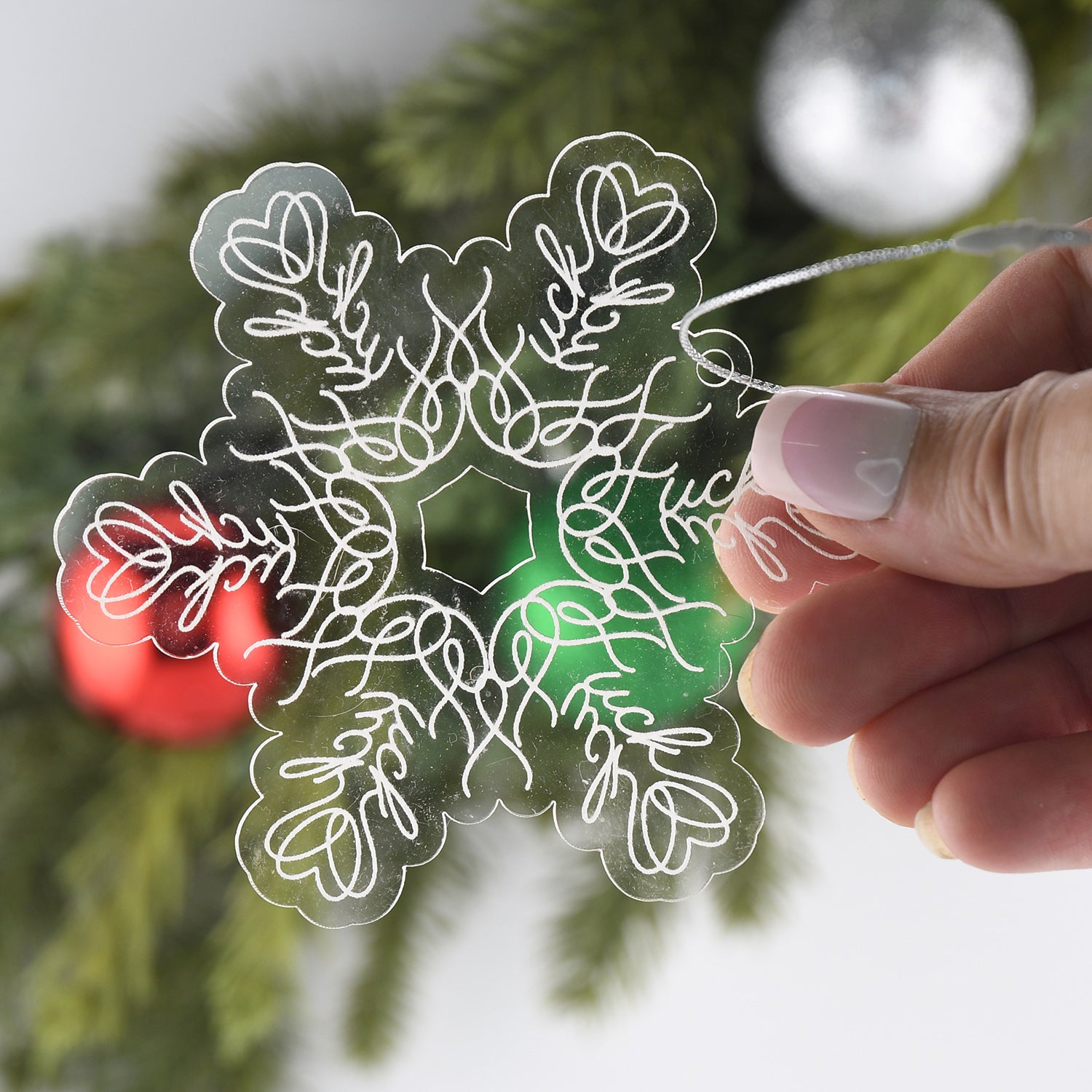 Acrylic ornament with hidden "fuck" words, on a blurred holiday background, held by a woman's hand.