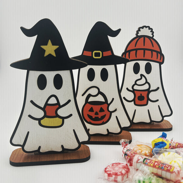 Three Halloween-themed ghost figurines with candy and pumpkins on a white background.
