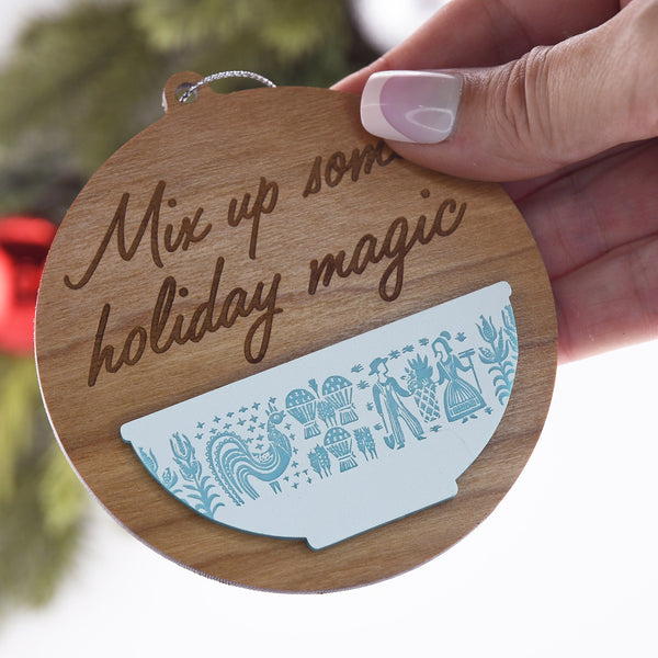 Wooden ornament with 'Mix up some holiday magic' text and decorative design, held by a hand.