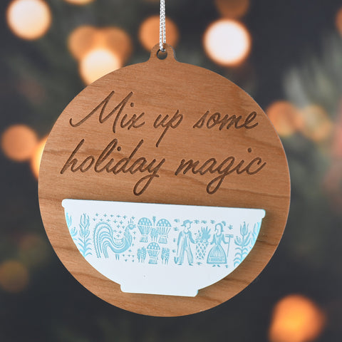 Wooden ornament with 'Mix up some holiday magic' text and a bowl design, against a blurred Christmas tree background.