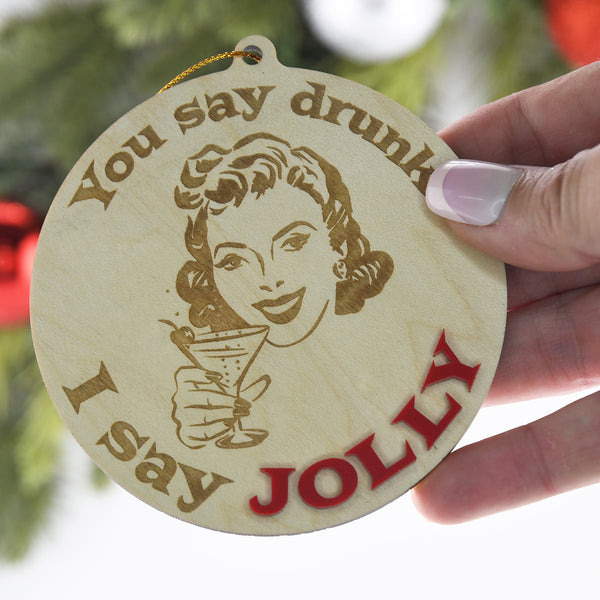 Wooden ornament with a woman holding a martini and text 'You say drunk, I say Jolly' held by a hand.