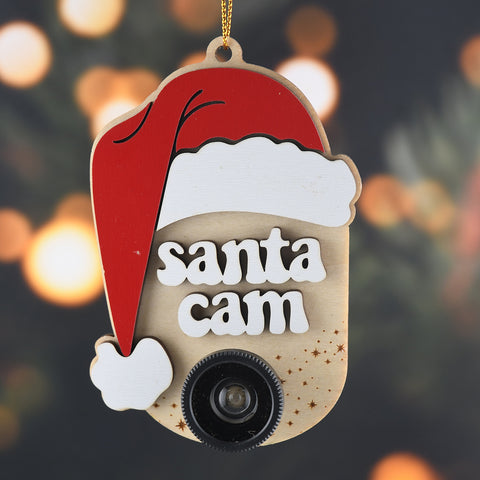 Ornament with a Santa hat, the words "Santa Cam" and a plastic camera lens hanging in front of a blurred background