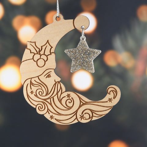 Decorative wooden ornament shaped like a crescent moon with a face, holly, and a star on a blurred festive background.