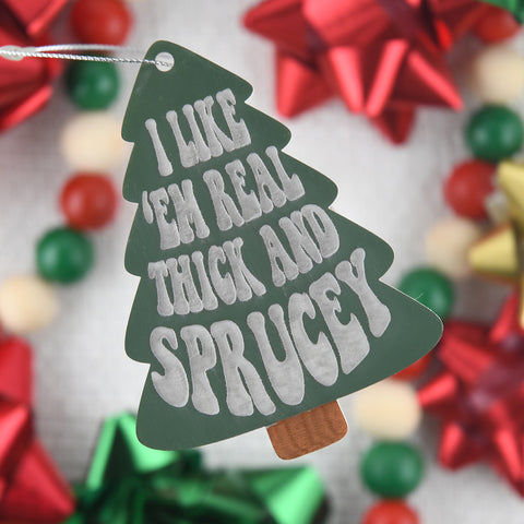 I Like em Real Thick and Sprucey ornament hanging in front of blurred bow background