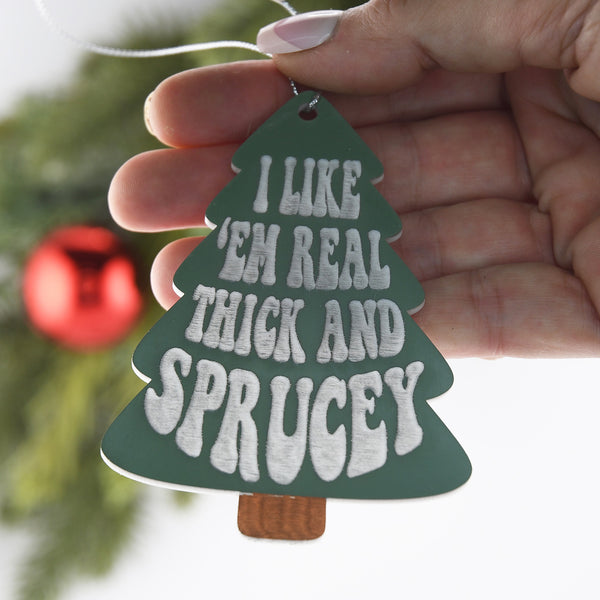 I Like em Real Thick and Sprucey ornament held in a woman's hand.