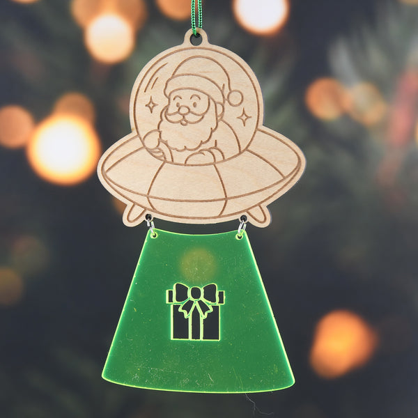 Decorative ornament with Santa Claus in an UFO and a green base with a gift icon, against a blurred Christmas tree background.
